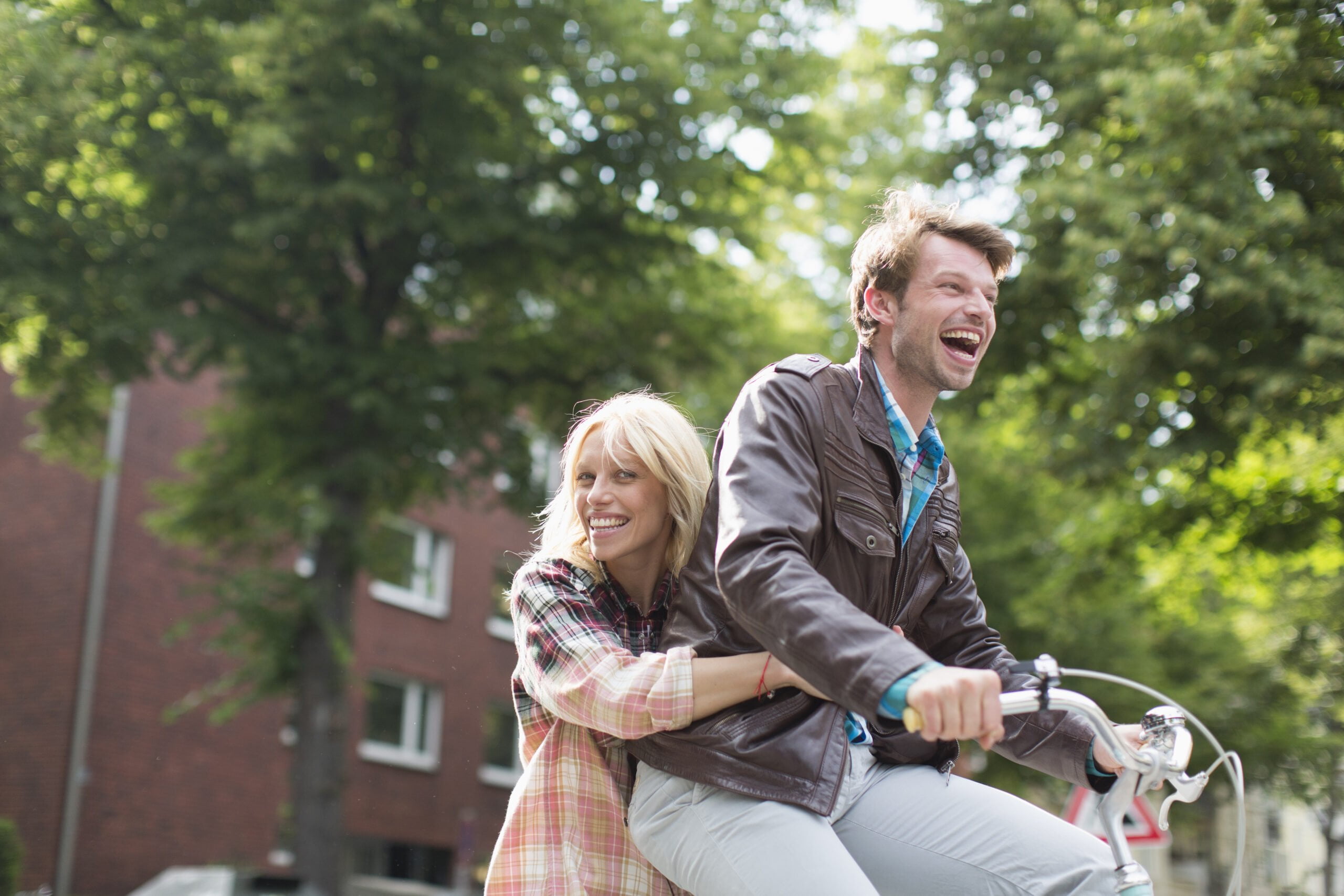 Happy playful young couple riding bicycle in park
